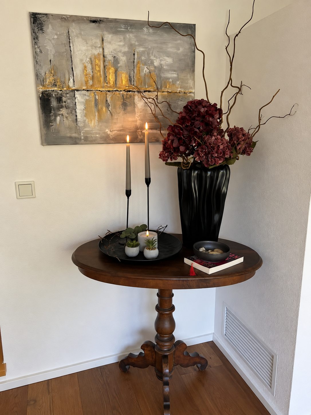 Runder Holztisch mit Kerzen, Blumen und Kunstwerk an der Wand